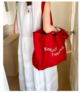 Detail of red canvas tote bag with Keep our free youth embroidery carried by a model