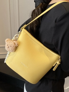 Borsa a secchiello minimalista in pelle gialla con trama litchi e ciondolo a orsetto