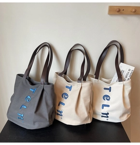 Three canvas tote bags in grey and cream with leather straps and blue 3D embroidery
