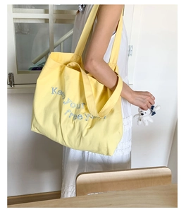 Detail view of blue embroidered Keep Your Free You text on yellow canvas tote bag