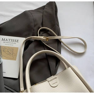 Gros plan sur le sac seau en cuir grainé blanc crème posé sur un blazer gris chic