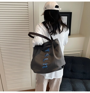 Detail view of a large canvas tote bag with blue teln embroidery worn by a model