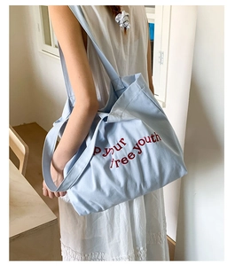 Detail of light blue canvas tote bag with red embroidered text on long shoulder strap