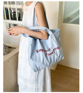 Lifestyle view of a large light blue canvas tote bag with red embroidered youth slogan