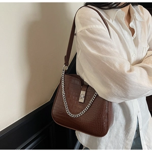 Detail view of dark brown crocodile pattern underarm bag with silver metal chain accessory