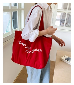 Detailed view of red canvas tote bag with Keep your youth free white embroidered letters