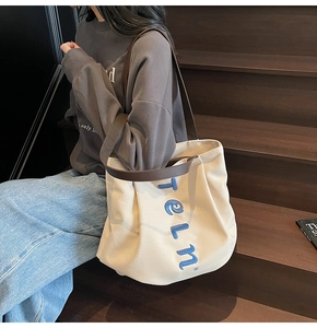 Close-up of cream canvas tote bag with blue teln embroidery and brown leather handle