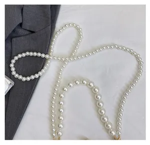 Detail of white pearl strap for handbag with golden clasps on textured background