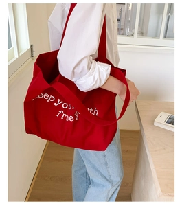 Detail of red canvas tote bag featuring white keep your free letter embroidery and texture