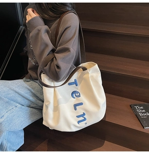 Detailed close-up of blue 3D embroidery on a cream canvas tote with brown straps