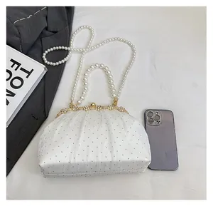 Macro view of white pleated evening bag with pearl chain and golden flower clasp detail