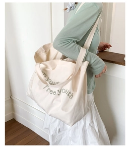 Detail of embroidered letters on a large cream canvas tote bag with shoulder straps