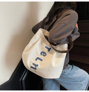 Detail of white canvas tote bag with brown webbing straps and blue embroidered lettering