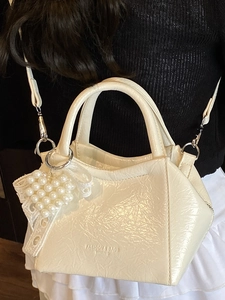 Borsa a secchiello minimalista beige con ciondolo a cuore di perla portata a tracolla
