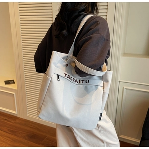 Detail view of canvas tote bag with letter embroidery and functional side pockets