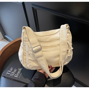 Close-up of white canvas crossbody bag with silver buckles and pleated details on strap