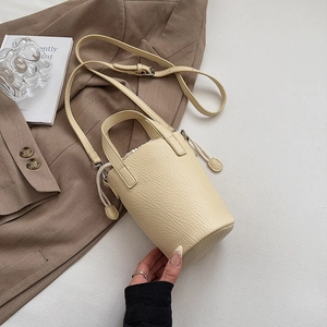 Detail view of beige litchi grain leather bucket bag with drawstring and top handles