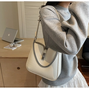 Detailed view of white crocodile pattern shoulder bag with silver buckle worn by a model