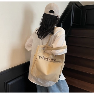 Detail of canvas tote bag showing side pockets, zippers, and large TAOCAITU lettering