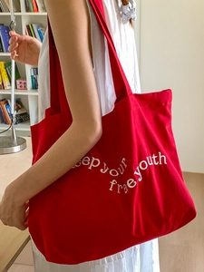 Red canvas tote bag with white letter embroidery shown in a lifestyle indoor setting