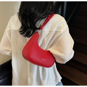 Gros plan sur un sac demi-lune rouge en cuir grainé porté par un mannequin en extérieur