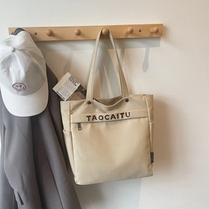 Detail of canvas tote bag showing side pocket, metal zipper front pouch, and brand lettering