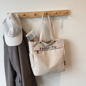Detail of beige canvas tote bag with brown TAOCAITU embroidery and side brand tag
