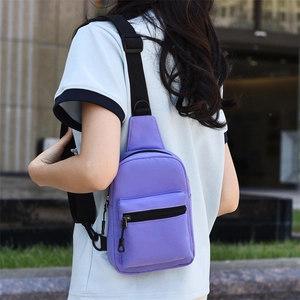 Detail view of purple canvas crossbody bag with adjustable strap worn by a person
