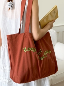 Red canvas tote bag with green letter embroidery on a white background with model