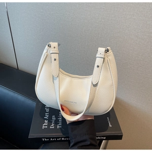 Gros plan du sac demi-lune ivoire en cuir à motif lychee sur un livre de design