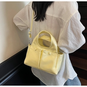 Detail of bright yellow patent leather tote bag with dual pockets and adjustable strap