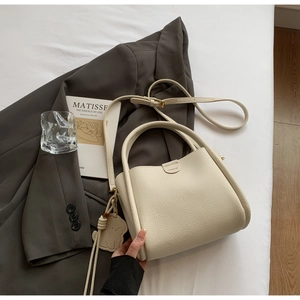 Détail du sac seau en cuir grainé crème avec poignée et pendentif ours décoratif