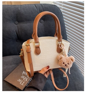 Detail of cream crocodile textured bucket bag with brown handles and a cute bear charm