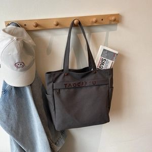 Detail of dark grey canvas tote bag with front zipper pocket and shoulder straps hanging