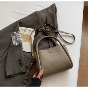 Détail du sac seau en cuir taupe avec poignée supérieure et pendentif ours décoratif