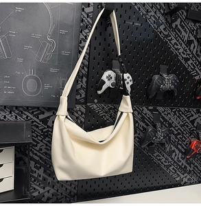 Detail of a creamy white PU leather tote bag with a black zipper against a dark industrial wall