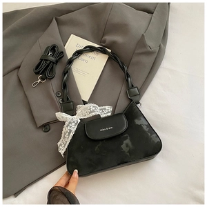 Detail view of black underarm bag featuring woven handle, lace bow, and adjustable strap
