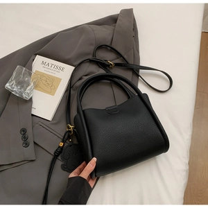 Détail d'un sac à main noir en cuir grainé avec breloque chien sur une veste grise
