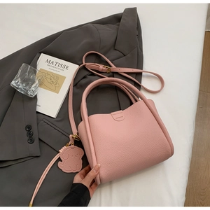 Vue détaillée d'un sac seau rose à grain de litchi avec un pendentif chien en cuir