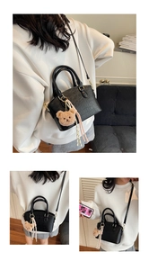 Detail of black crocodile texture bucket bag with a cute bear charm and golden hardware