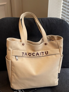 Minimalist beige canvas tote bag with letter embroidery on a blue corduroy sofa