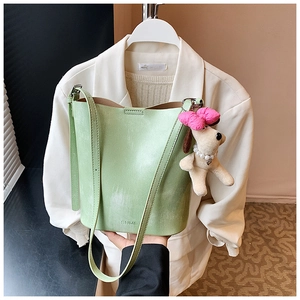 Detail der hellgrünen Beuteltasche mit Plüschwelpen-Anhänger vor weißem Blazer-Hintergrund