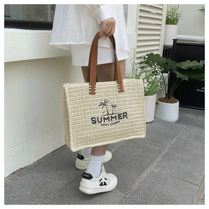 Close-up of large straw tote bag with palm tree embroidery and leather handles
