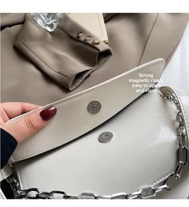 Detail of silver magnetic buckle closure on a white patent leather baguette bag