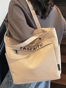 Off-white canvas tote bag with brown embroidery and zipper pocket, modeled on shoulder