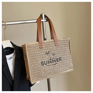 Detail of woven straw tote bag with black Summer embroidery and brown leather handles