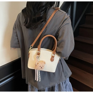 Detail showing white crocodile embossed bucket bag with brown strap and plush bear charm