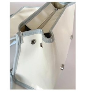 Détail du sac à dos beige montrant le bouton-pression argenté et les finitions bleues