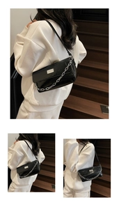 Detailed view of black patent leather baguette bag featuring silver chain and metal plate