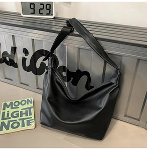 Detail view of a large black matte leather hobo bag against an industrial background